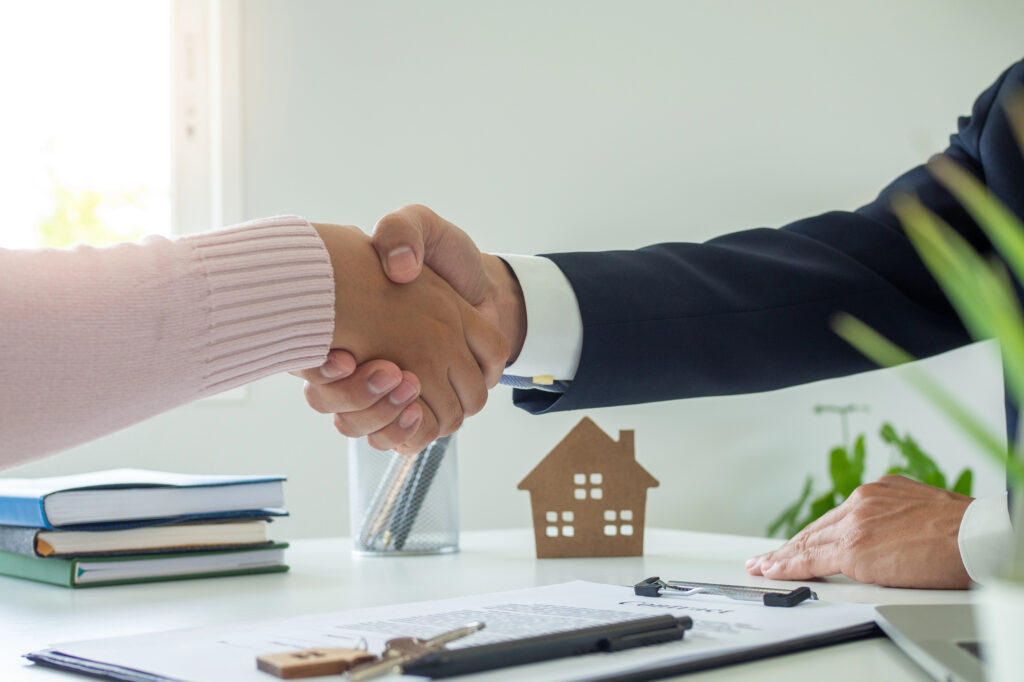 Two people shaking hands over a desk and paperwork